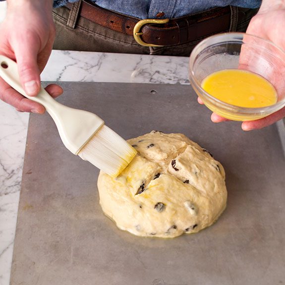 Person using a brush to put an egg wash over the soda bread dough