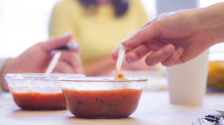 Two hands reaching out to spoons sticking out of two separate plastic bowls of salsa