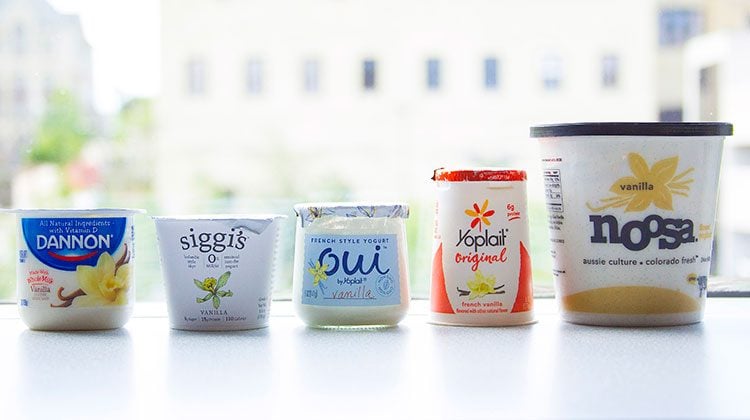 5 different brands of yogurt containers lined up in front of a window