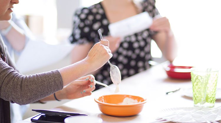 Person holding a spoon of yogurt over an orange bowl letting excess yogurt drip down