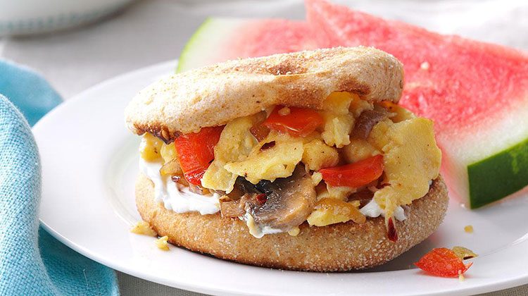 English muffin with scrambled eggs mixed with red peppers and mushroom slices in between its two halves