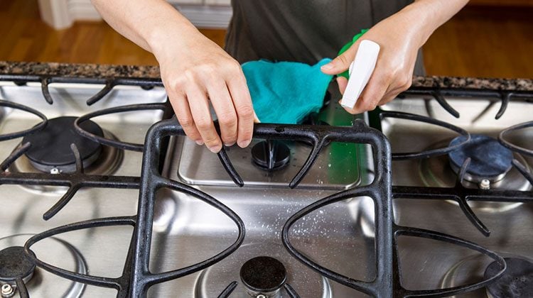 Person lifting up the black grating of their stovetop to spray cleaner underneath it from a spray bottle