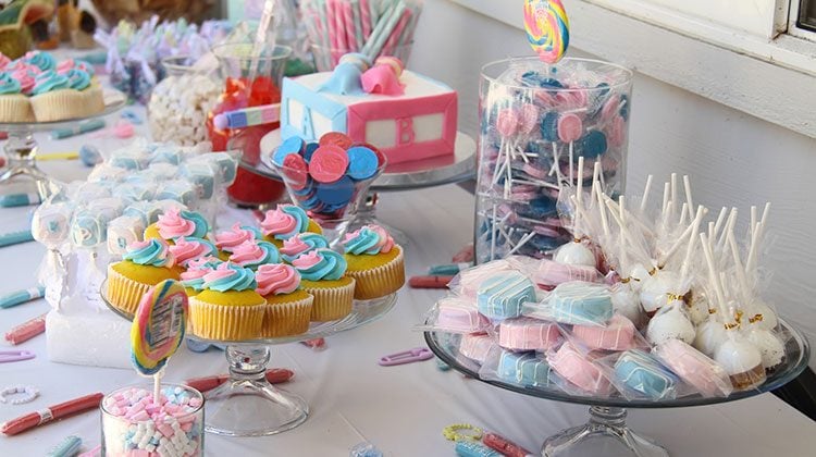 Table filled with glass platters holding pink and blue frosted cupcakes, cake pops, and other assorted candies in glass jars