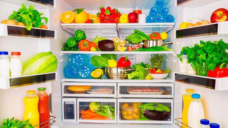 Double-door fridge open wide and filled to the brim with fresh vegetables, fruit, bottles of water and jugs of milk