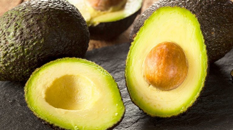 Avocados piled together with one sliced in half and propped up to reveal its insides to the viewer