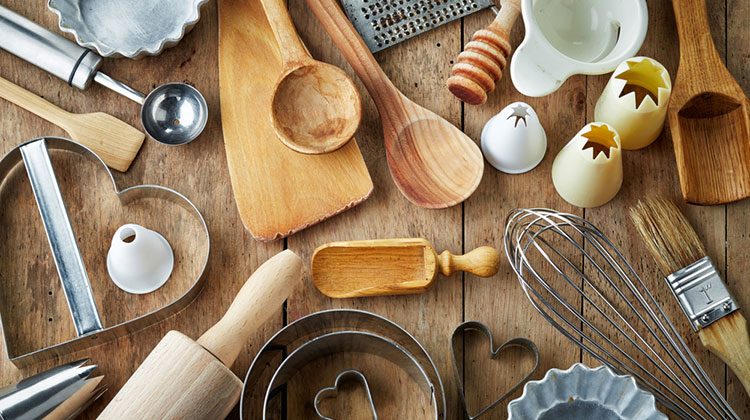 Kitchen tools of all shapes and sizes spread out in an organized mess on a wooden counter