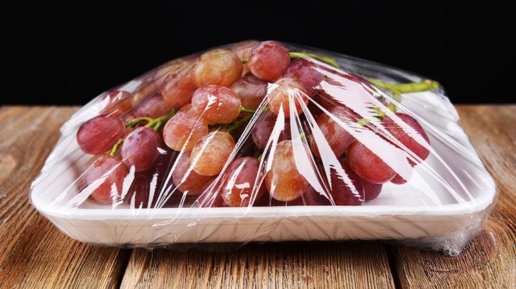 A bunch of grapes on a styrofoam tray covered in saran wrap on a wooden table