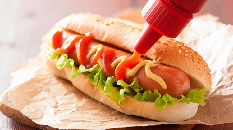 Bottle of ketchup squirting a serpentine line across a hotdog