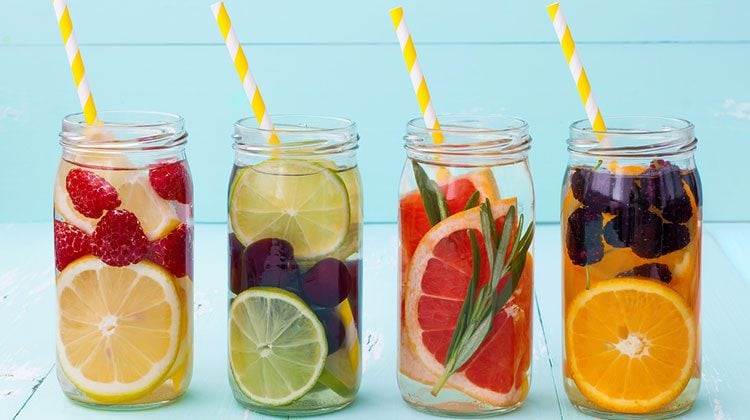 Four glass jars each with a different combination of sliced fruit and whole berries plus yellow-striped straws