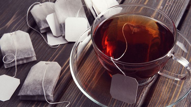 Glass cup filled with tea surrounded by tea bags on a wooden countertop