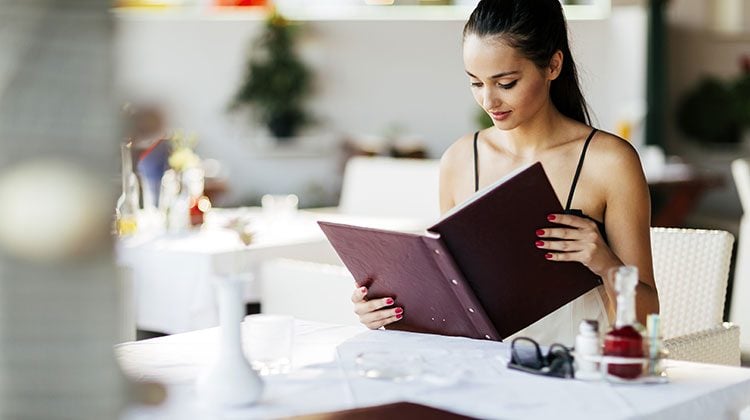 Woman in a black tank top looking over a menu as she sits at a table with a white tablecloth