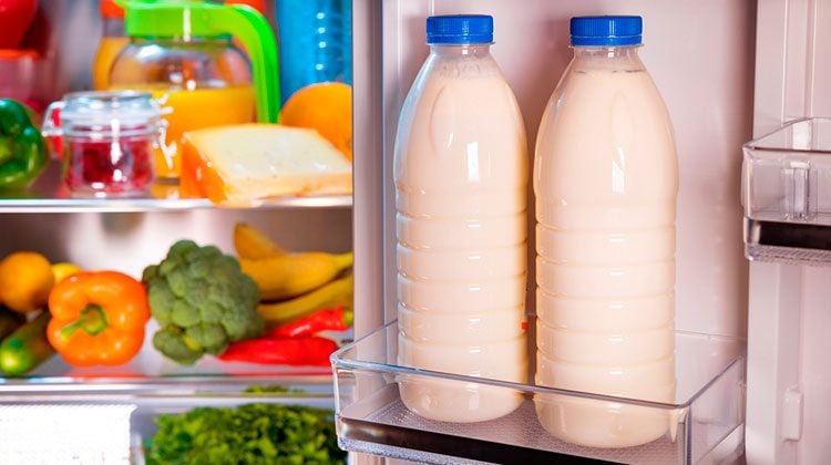 Two full jars of milk sit in the door shelf of the fridge door and the shelves are filled with produce