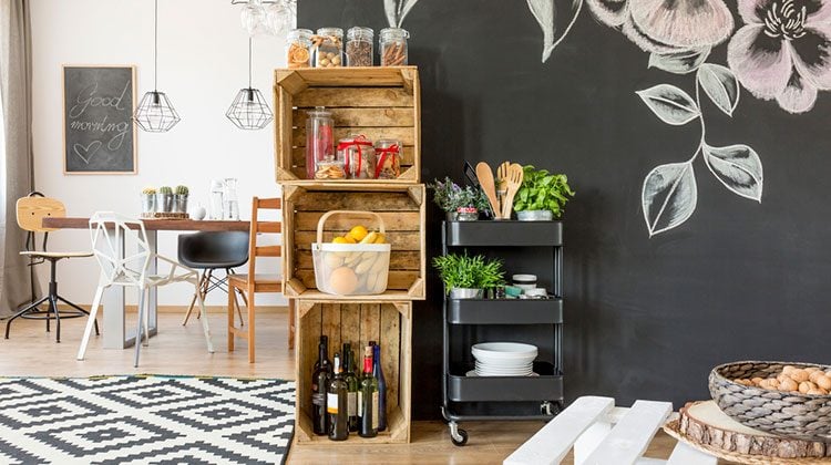 Large, well organized kitchen featuring crates used as shelves, floral patterns on black walls and a modern style kitchen table with four completely different chairs gathered around it