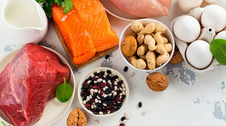 Raw fish, chicken and beef in white bowls beside a carton of eggs and bowls of different beans and nuts