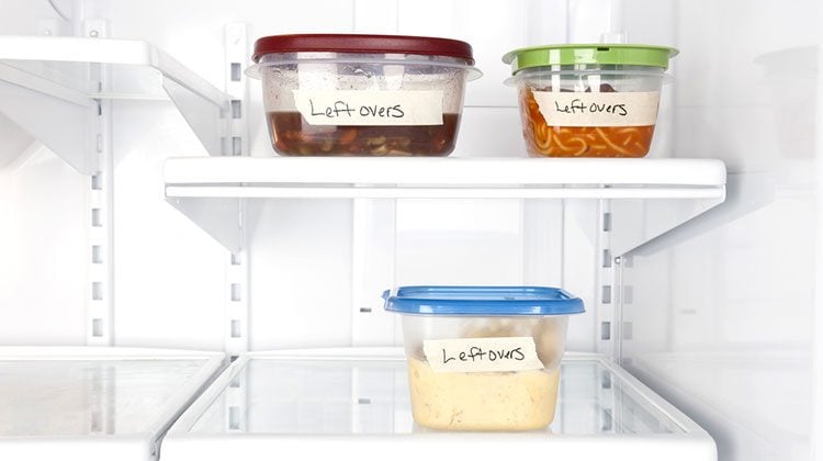 Fridge with three tuber ware containers inside, each with a different colored lid and labelled with the word 'leftovers'