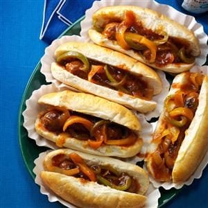 Five Barbecue Brats & Peppers in individual papers and lined up on a teal plate, which they barely fit on, on top a bright blue table