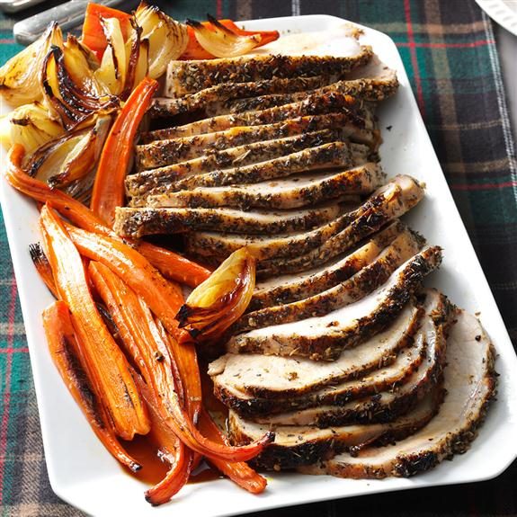 Thick slices of Italian Herb-Crusted Pork Loin lined up on a rectangular white plate with roasted veggies lining the left side