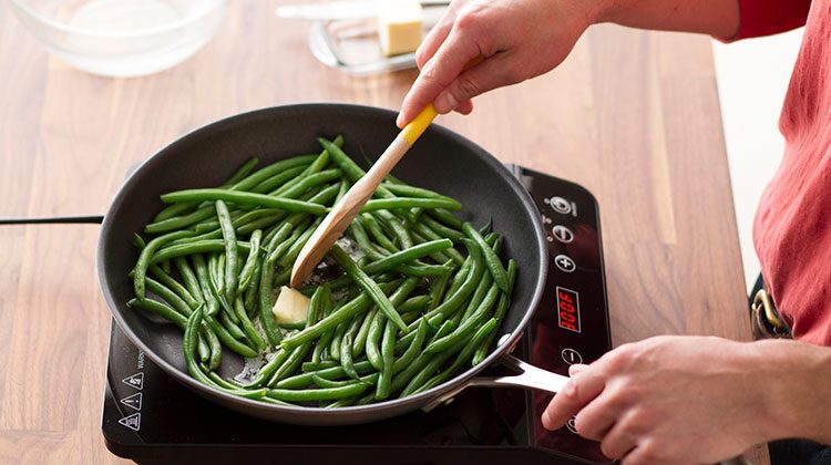 Person stirring a slice of butter into their green beans as they cook in a skillet