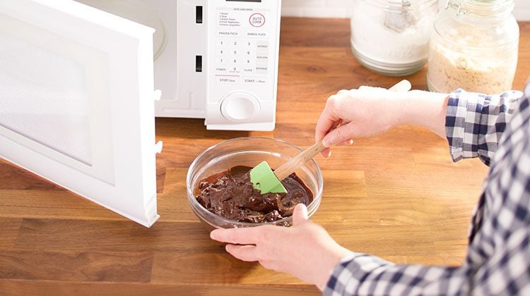 Person using a green spatula to stir melting chocolate in a bowl straight from their now open microwave