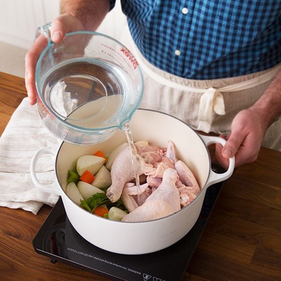 Chicken and vegetables together in a large pot as a person pours water over them