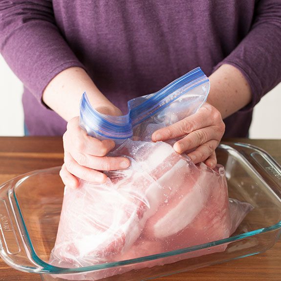 Person sealing a bag of raw pork chops closed