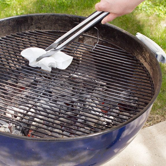 Person using metal tongs to rub paper towel against their grill