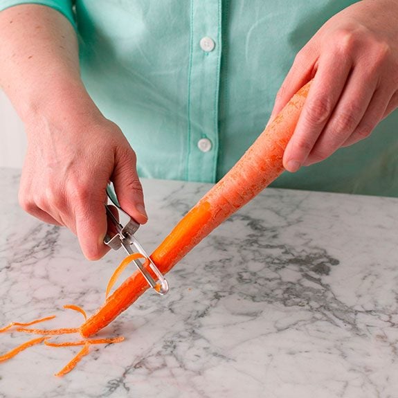 person holding a carrot and peeling the tip