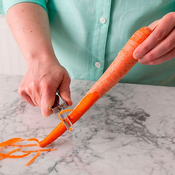 person holding a carrot and peeling the tip