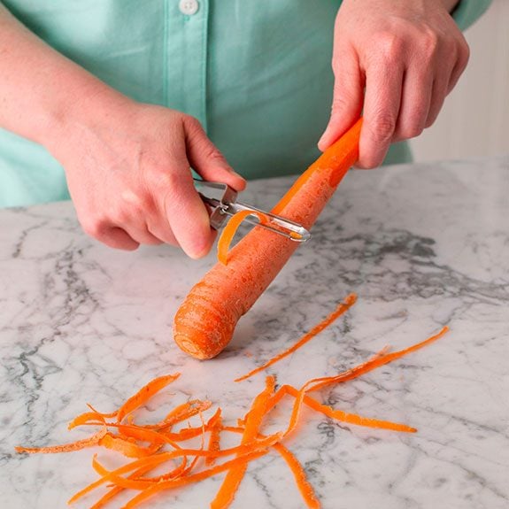 person holding a carrot and peeling from the center to the end