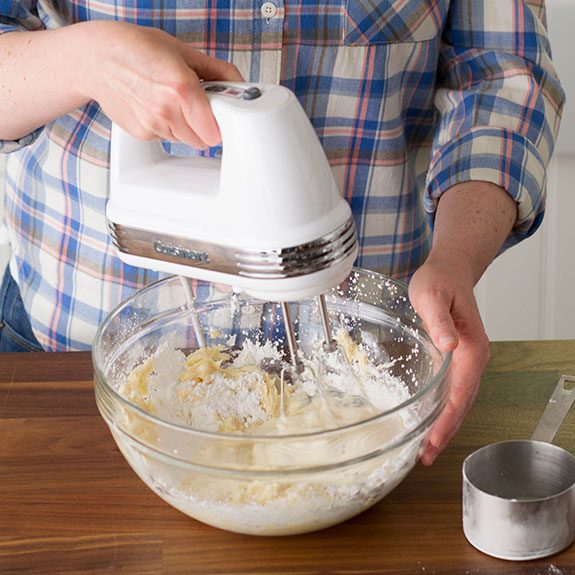 Person just beating the sugar into the mixture with a hand mixer with a metal measuring cup nearby