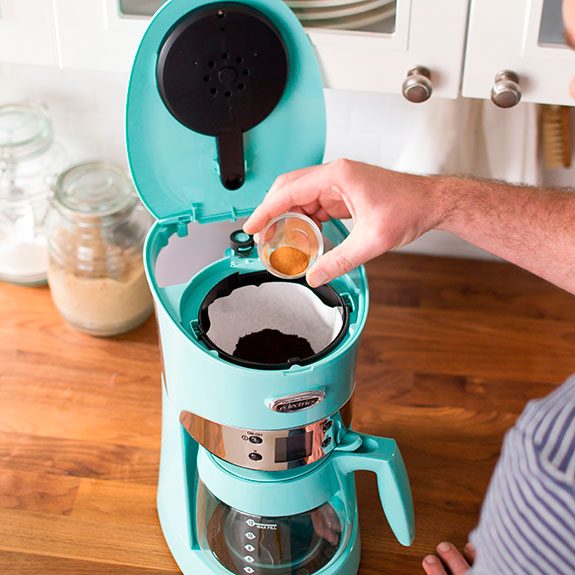 Person pouring spice into the top compartment of a bright blue coffee maker