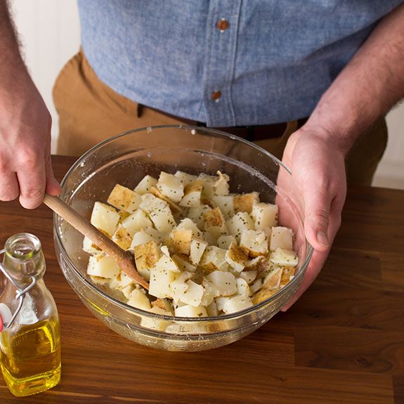 Cubed potatoes in a glass bowl being stirred and covered with oil