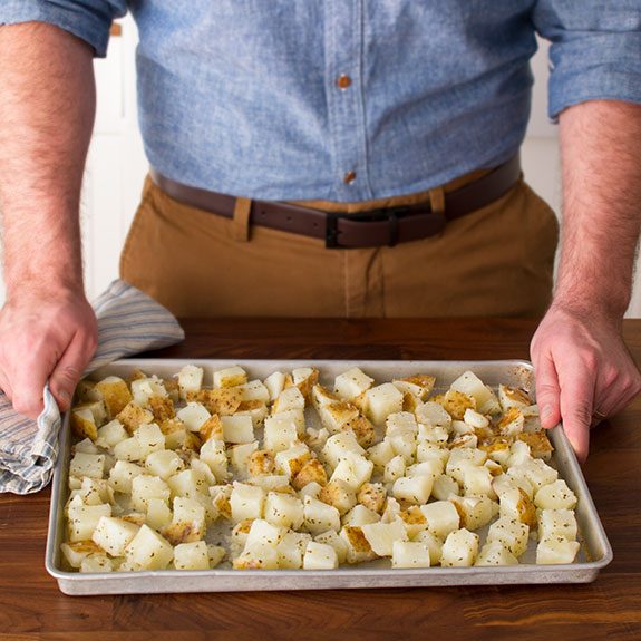 Baking sheet covered with cut, seasoned potatoes