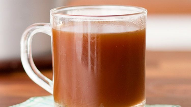 Glass mug filled with beef broth on top a wooden dining table