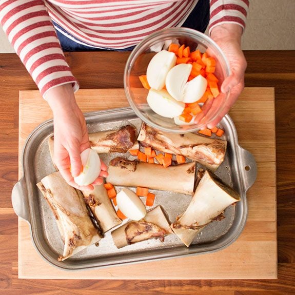 The bones from the stockpot are now laid out on a baking sheet and being covered with diced carrots and onions