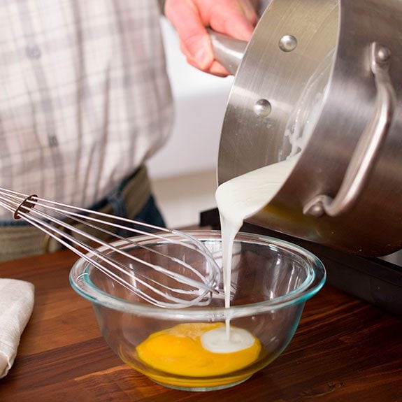 A person carefully pouring some of the mixture into a bowl of egg yolk