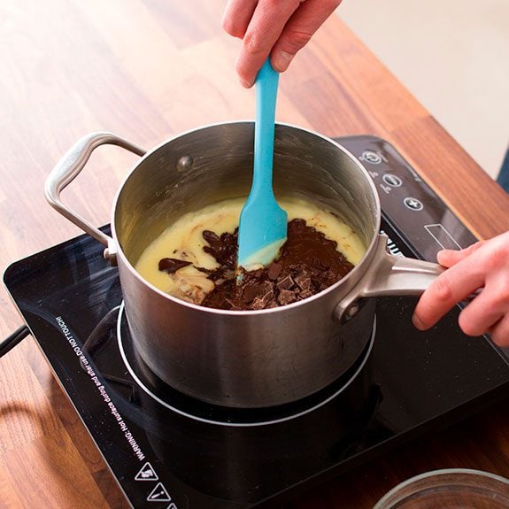 Stirring the pudding with a blue spatula to mix in the chunks of melting chocolate