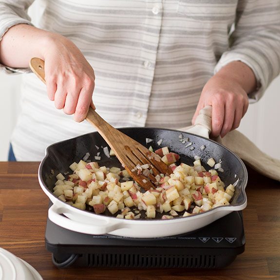 Potatoes, onions, and meat together in a skillet being stirred with a wooden spoon