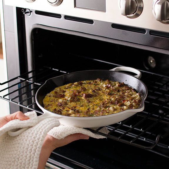 The semi-cooked frittata being put into a open oven to finish cooking while still in the skillet