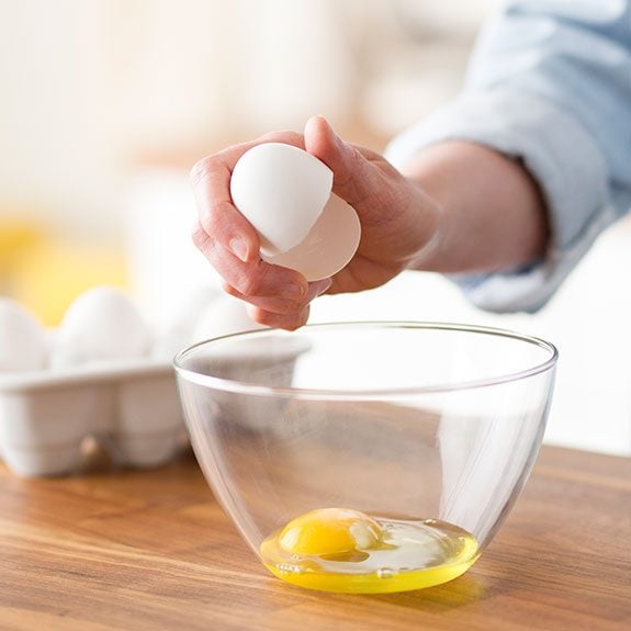 Hand holding a egg cracked perfectly in half over a bowl