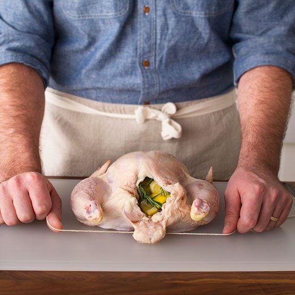 Person holding a string underneath uncooked, stuffed chicken