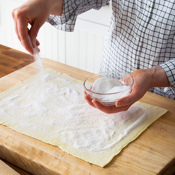 person sprinkling sugar onto a rectangle of dough