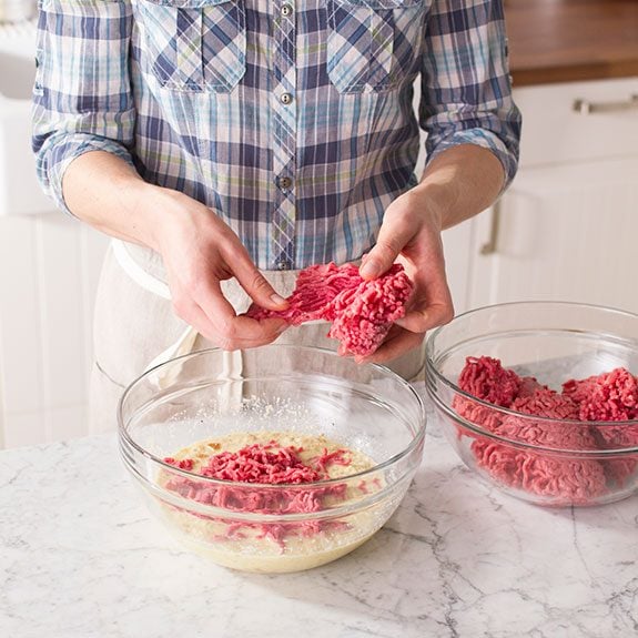 Person using their hands to combine the ingredients for the meatballs across two glass bowls