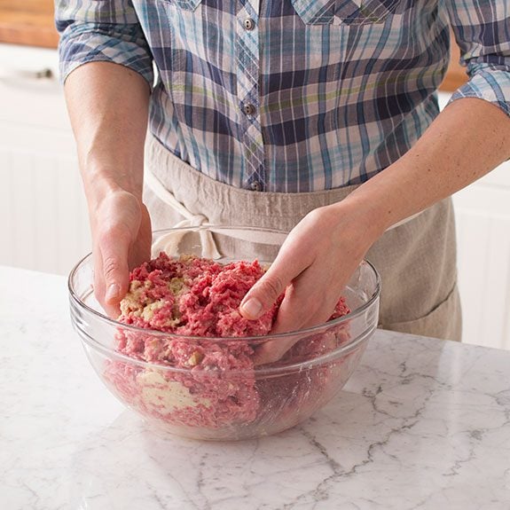 Person using their hands to combine the ingredients for the meatballs in one large glass bowl