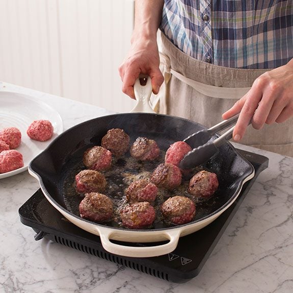 Using tongs, the person then transfers their meatballs into a saucepan to brown them